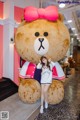 A woman posing in front of a giant teddy bear.