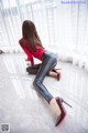 A woman in a red shirt and black leather pants crouching on the floor.