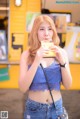 A woman in a blue top and jeans eating a sandwich.