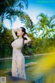 A woman in a white dress standing next to a pool.