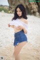 A woman in a white shirt and denim shorts posing on a beach.