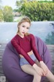 A woman sitting on a purple bean bag chair by a pool.