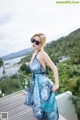 A woman in a blue dress and sunglasses standing on a balcony.