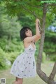 A woman in a white dress standing next to a tree.