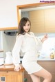 A woman in a white dress posing in a kitchen.