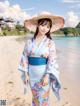 A woman in a blue kimono and a straw hat on the beach.