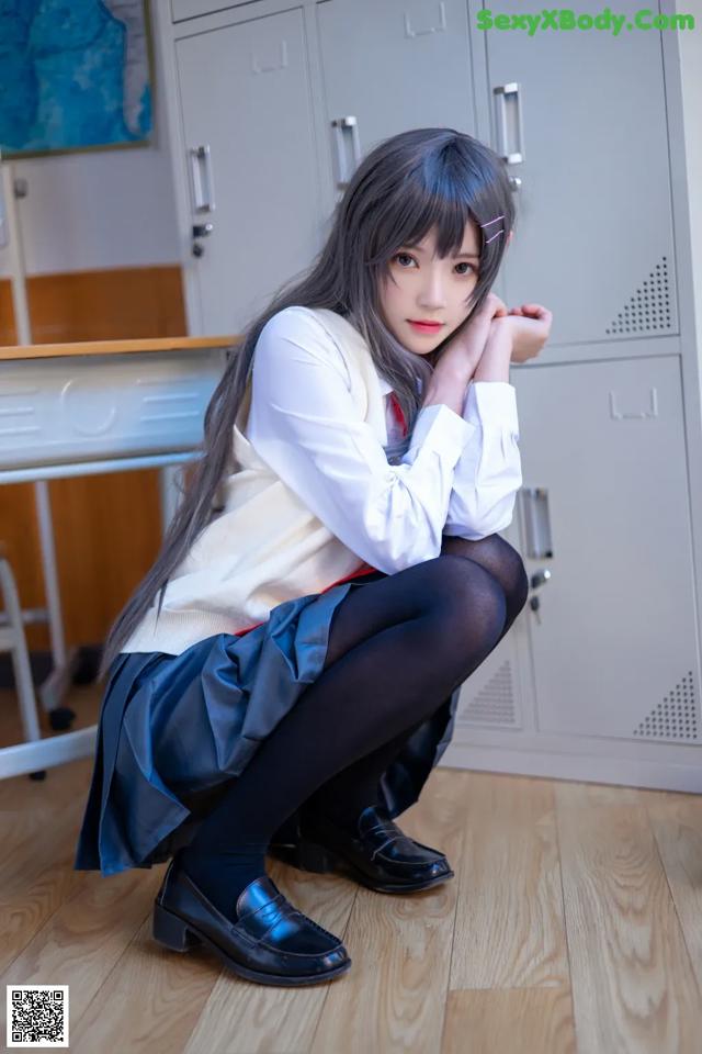 A woman in a school uniform sitting on the floor.