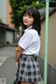 A woman in a white shirt and plaid skirt posing for a picture.