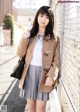 A young woman leaning against a fence wearing a coat.