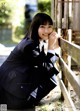 A woman in a school uniform leaning against a fence.