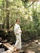 A woman in a white kimono standing on a wooden bridge.