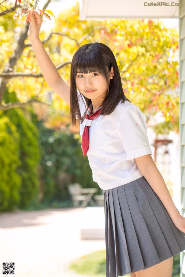 A woman in a school uniform holding a branch of a tree.