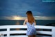 A woman in a blue and white dress looking out over the ocean.