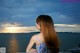 A woman with long red hair standing on a balcony overlooking the ocean.