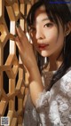 A woman in a white dress leaning against a wooden wall.