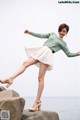 A woman in a green sweater and white skirt posing on a rock.