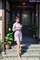 A woman standing in front of a house holding a cell phone.