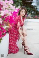 A woman in a red dress sitting on a wall with pink flowers.